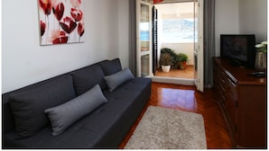 A modern living room with a dark sofa, a television, and a painting on the wall. - Apartment Slavko (Primosten)