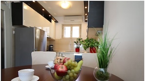 A dining area with a wooden table, a bowl of fruit, a cup, and a potted plant. - Apartment Slavko (Primosten)