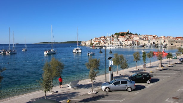 A coastal town with a marina, parked cars, and a pedestrian walkway along the water. - Apartment Slavko (Primosten)