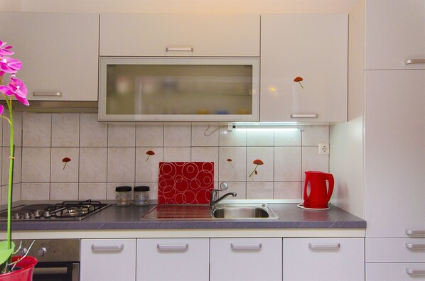 A kitchen with white cabinets, a stainless steel sink, a red kettle, and a gas stove. - Apartment Jema (Okrug Gornji)