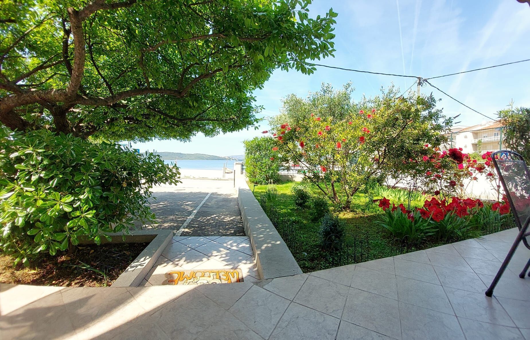 A pathway leading to a beach with lush greenery and red flowers.