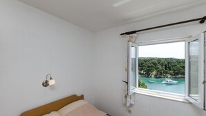 A bedroom with a bed, a window with curtains, a wall-mounted light, and a view of boats on water. - Apartments Katja (Primosten)