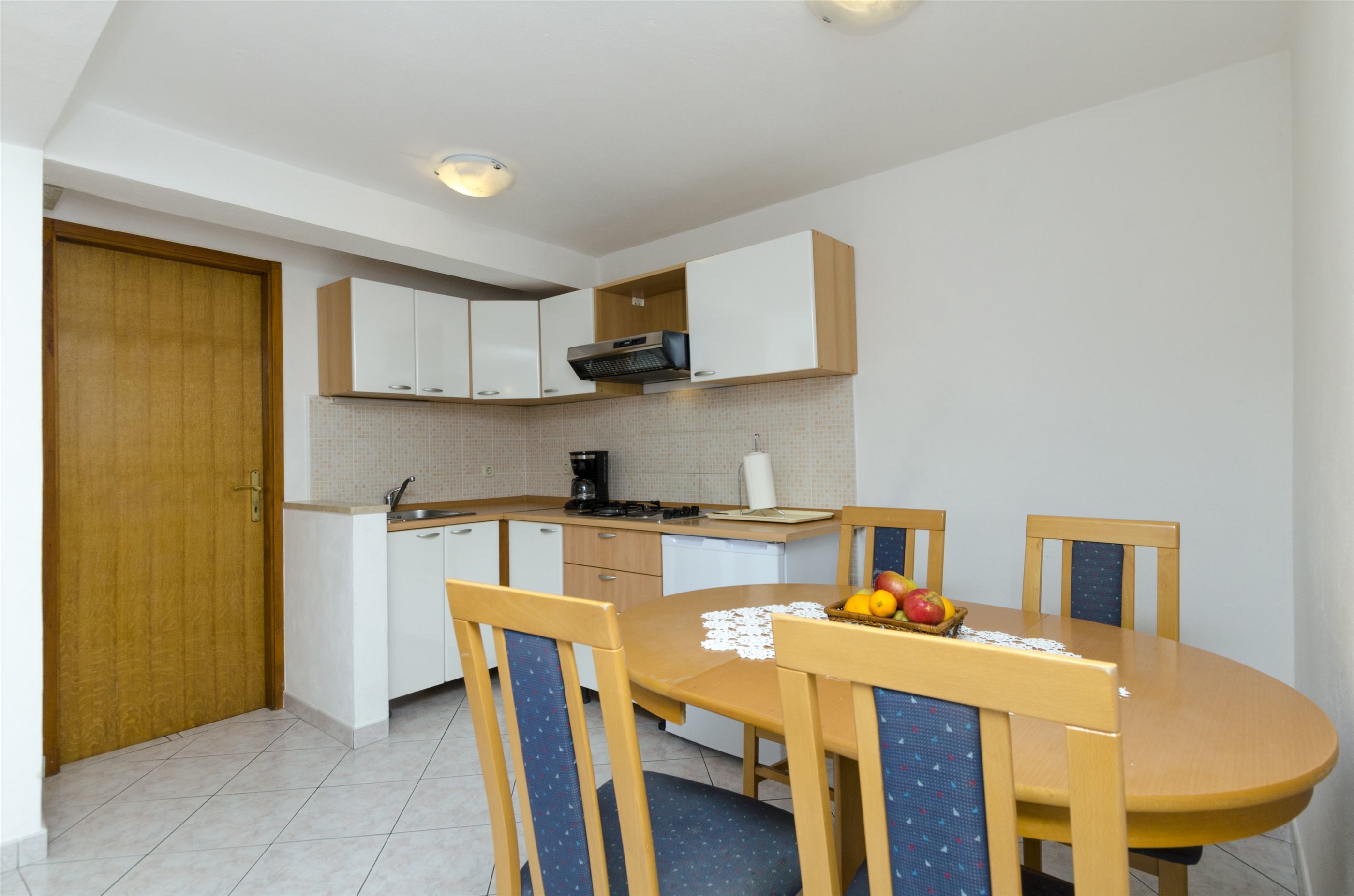 Una cocina compacta con armarios blancos, una puerta de madera y una mesa de comedor con sillas.