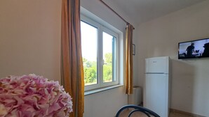 A room with a window, a television mounted on the wall, a white refrigerator, and a chair. - Apartments Karmen A1-A3 (Primosten)
