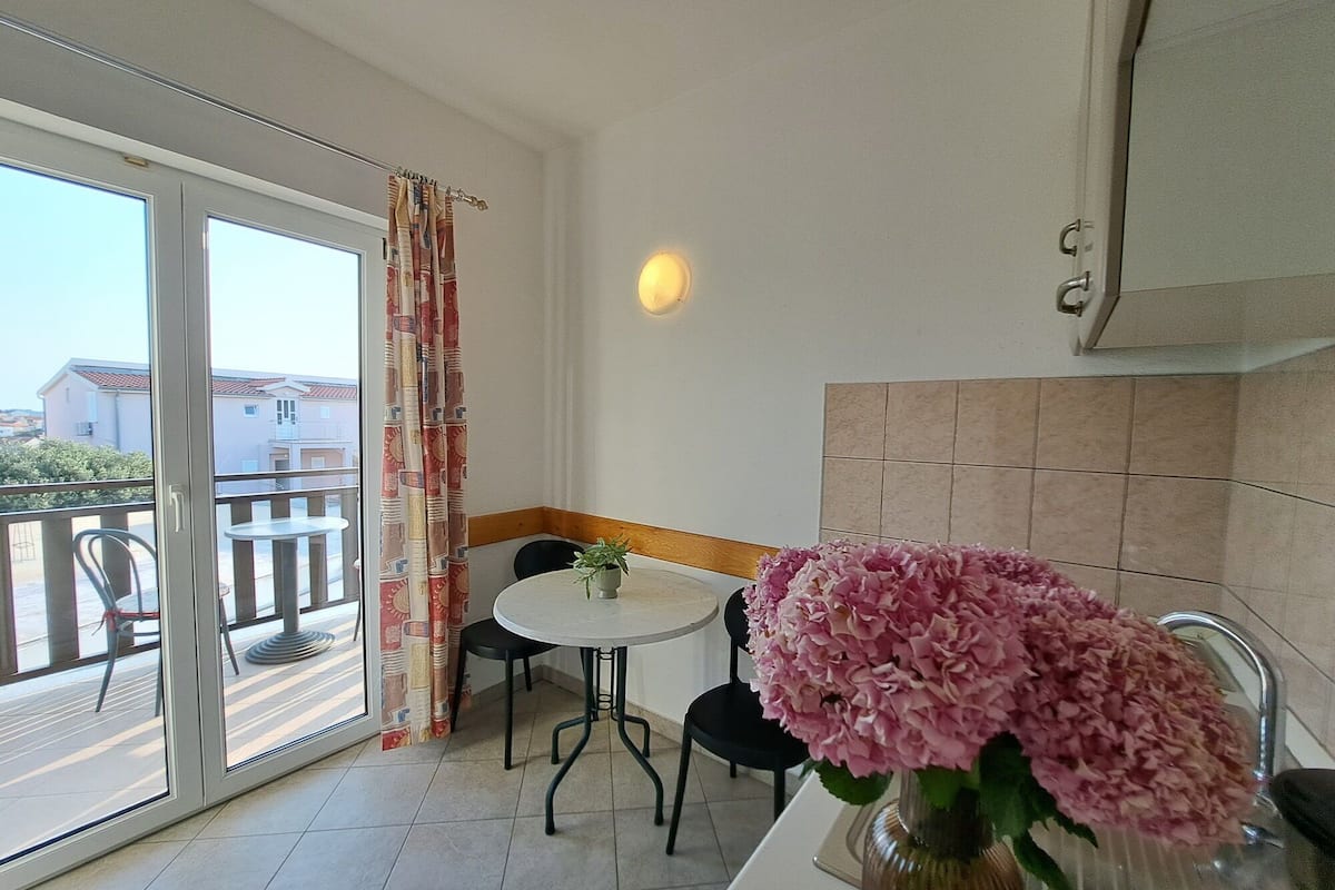 En balkon med spisebord, stole, en potteplante og en vase med lyserøde blomster.