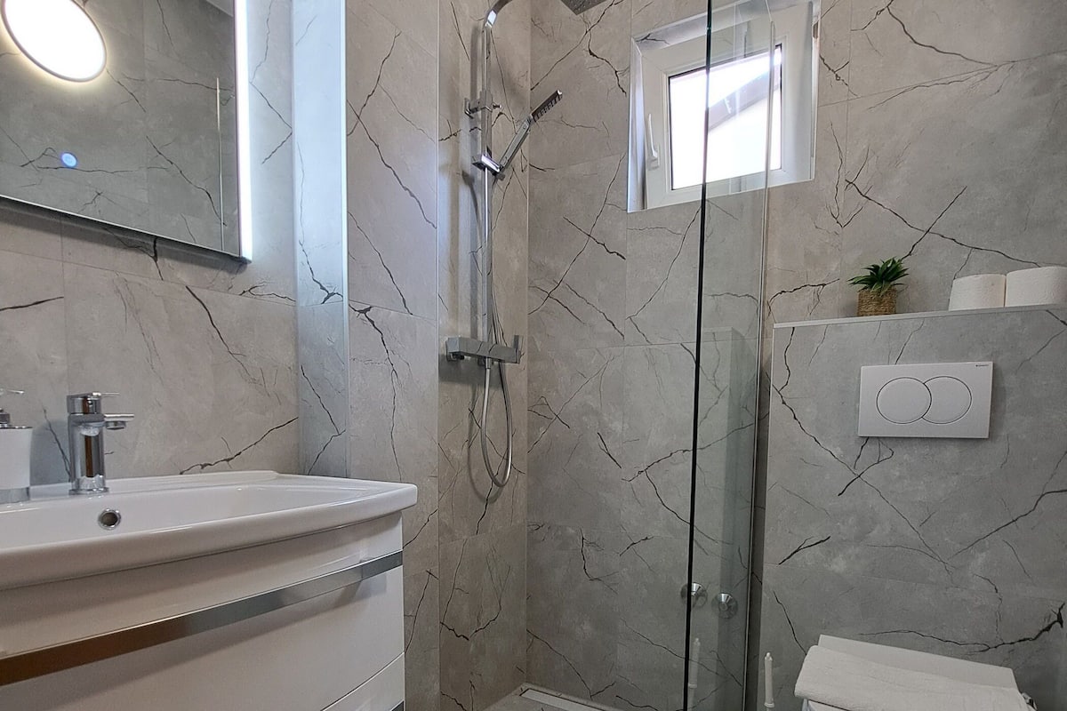 Et moderne badeværelse med et marmorgulv, en glasafskærmet brusekabine, en hvid vask og et toilet.