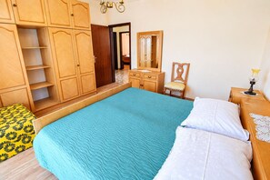 A bedroom with a large bed, wooden wardrobe, a dresser, a chair, and a bedside table with a lamp. - Apartment Lele (Primosten)