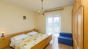 Une chambre à coucher avec un lit en bois, des tables de chevet, un lustre, une fenêtre avec des rideaux et un banc bleu.