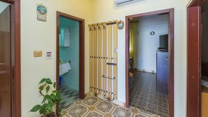 Un couloir avec un sol carrelé, une plante en pot, un climatiseur fixé au mur et une porte avec un porte-serviettes.