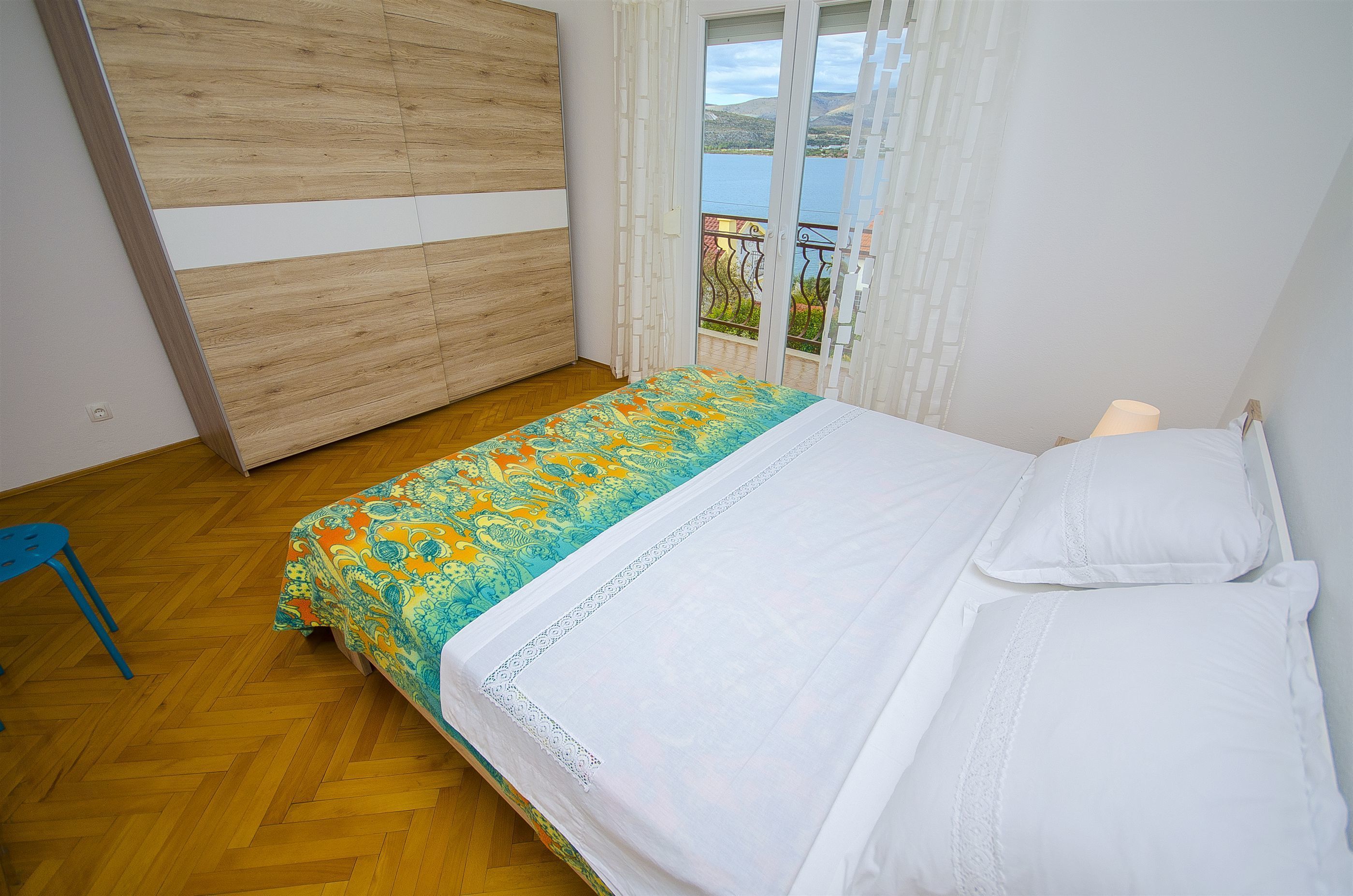 Ein Schlafzimmer mit einem Bett, einem Holzschrank, einem Balkon mit Seeblick und einem blauen Stuhl.