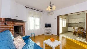 A living room with a blue sofa, a white coffee table with oranges, a brick fireplace, and a TV on a stand. - House Marija (Arbanija)