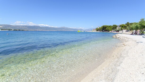 A clear beach with a calm sea, a sandy shore, and a distant mountain range. - House Marija (Arbanija)