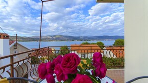 A balcony with a view of a lake and mountains, featuring a railing and a vase of pink flowers. - House Marija (Arbanija)