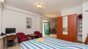Een hotelkamer met een bed, een bureau met een computer, een rode fauteuil, een houten garderobe en een televisie.