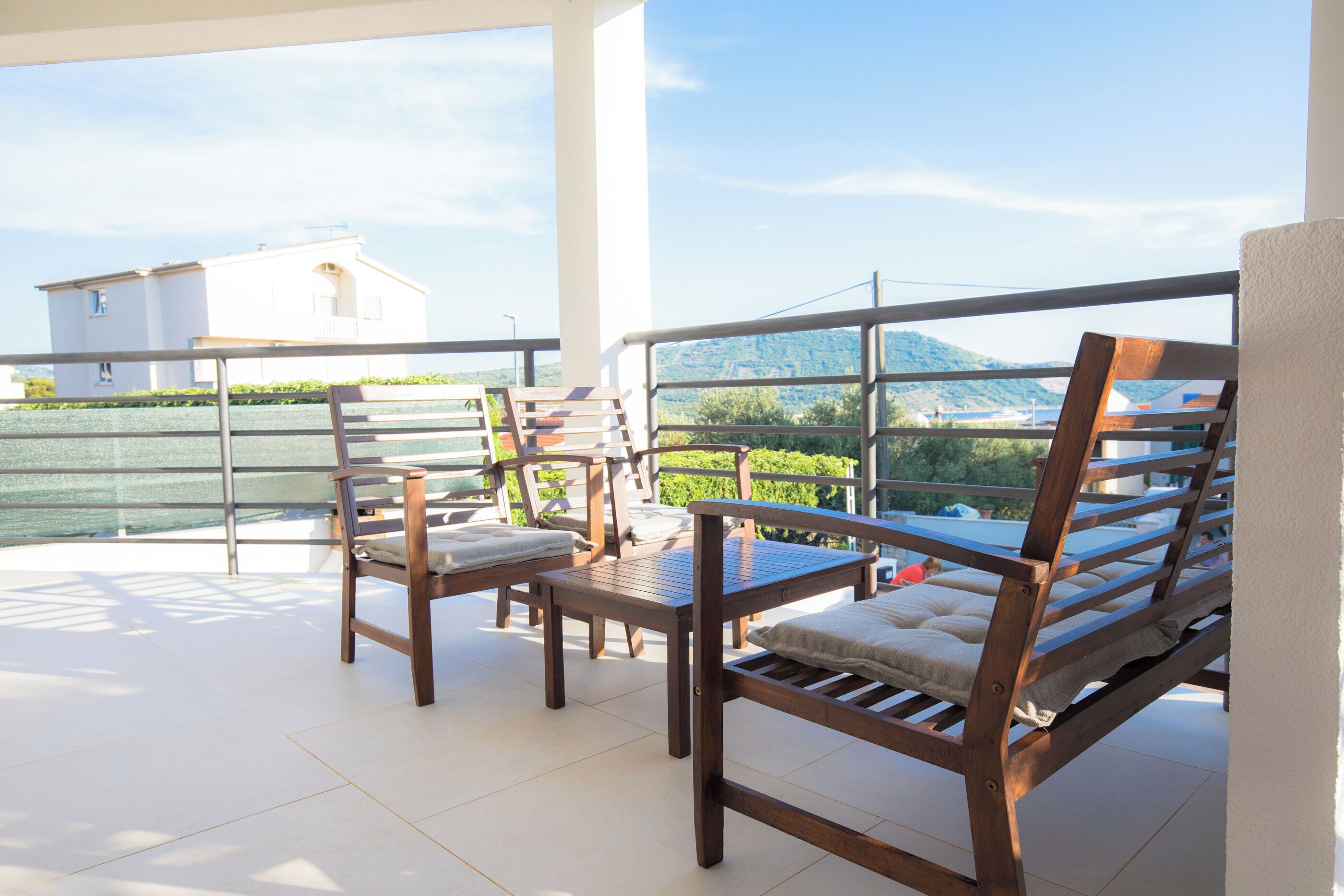 A balcony with wooden furniture and a view of a mountain and a building.
