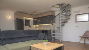 Ein modernes Wohnzimmer mit einer Couch, einem Couchtisch, einer Wendeltreppe und einer Küchenzeile.