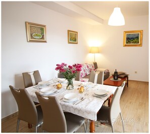 A dining area with a table set for four, surrounded by chairs. There is a vase with flowers on the table, and a lamp on the wall.