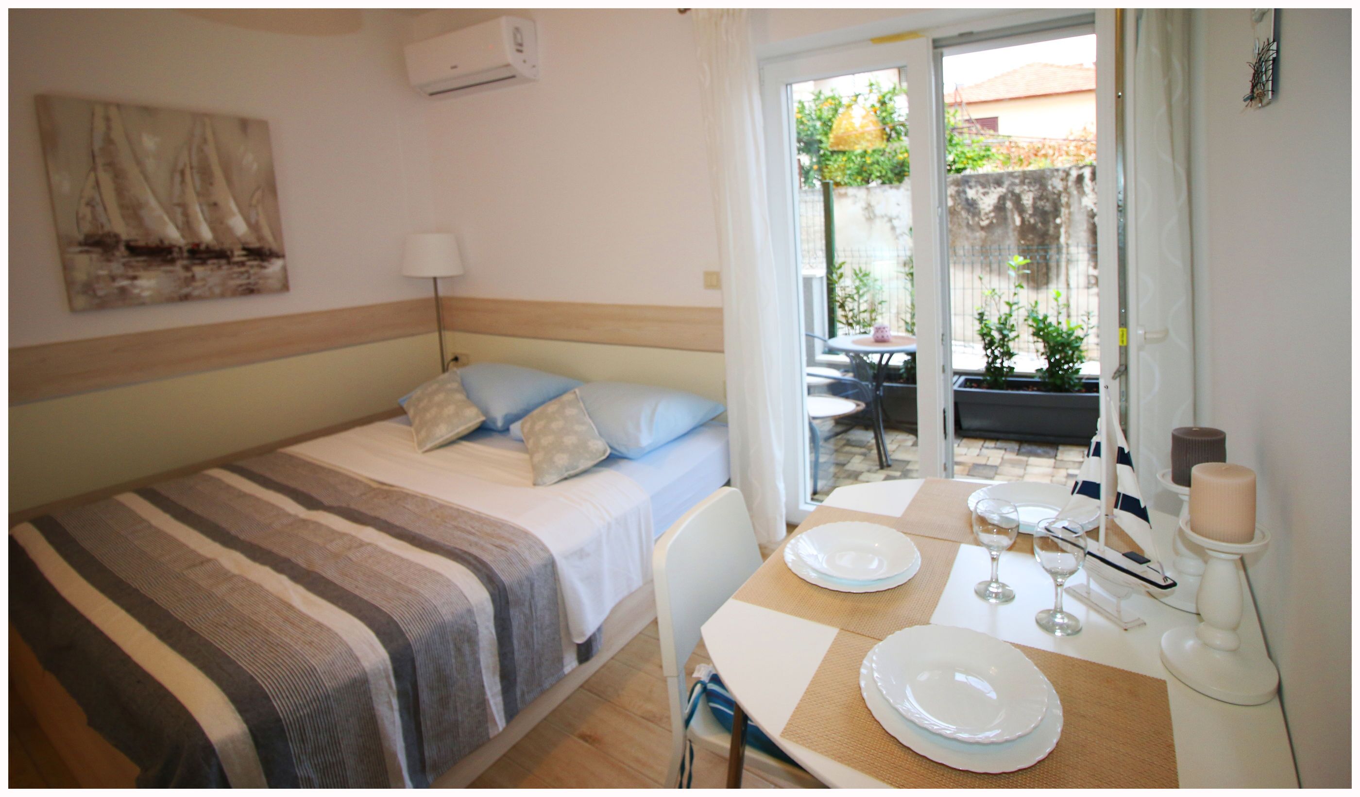 A bedroom with a bed, a table set for dining, and a view of the outside.