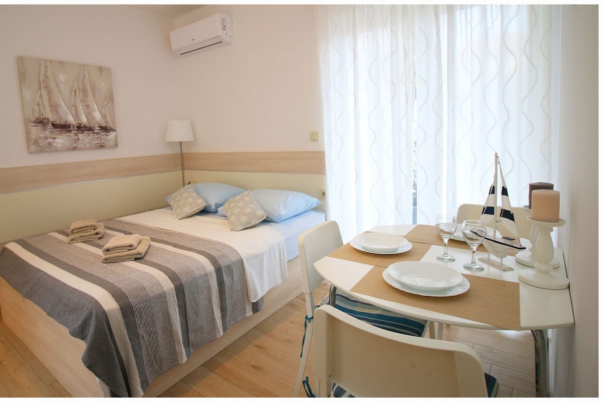 A hotel room with a bed, a small table with plates and a candle, and a window with curtains.