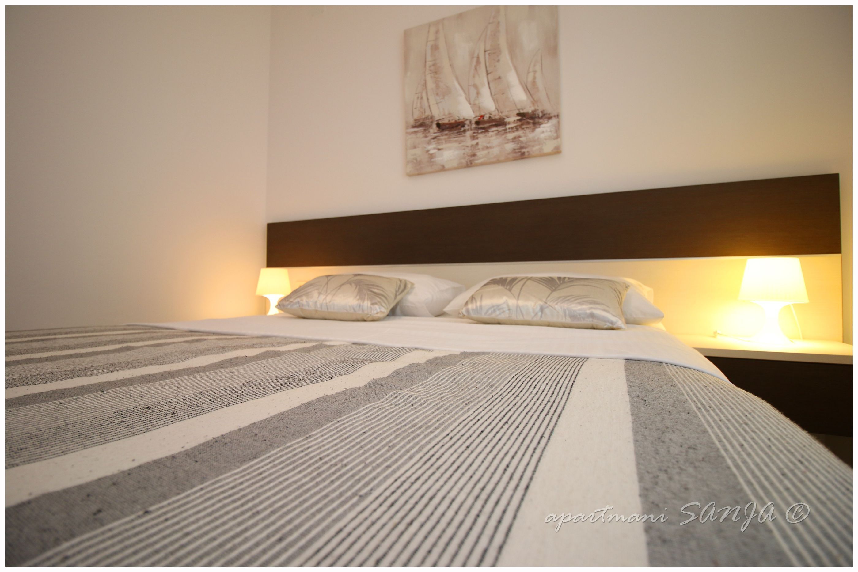 A neatly made bed with striped bedding, a headboard, and two bedside lamps.