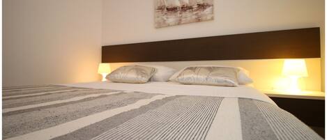 A neatly made bed with striped bedding, a headboard, and two bedside lamps.