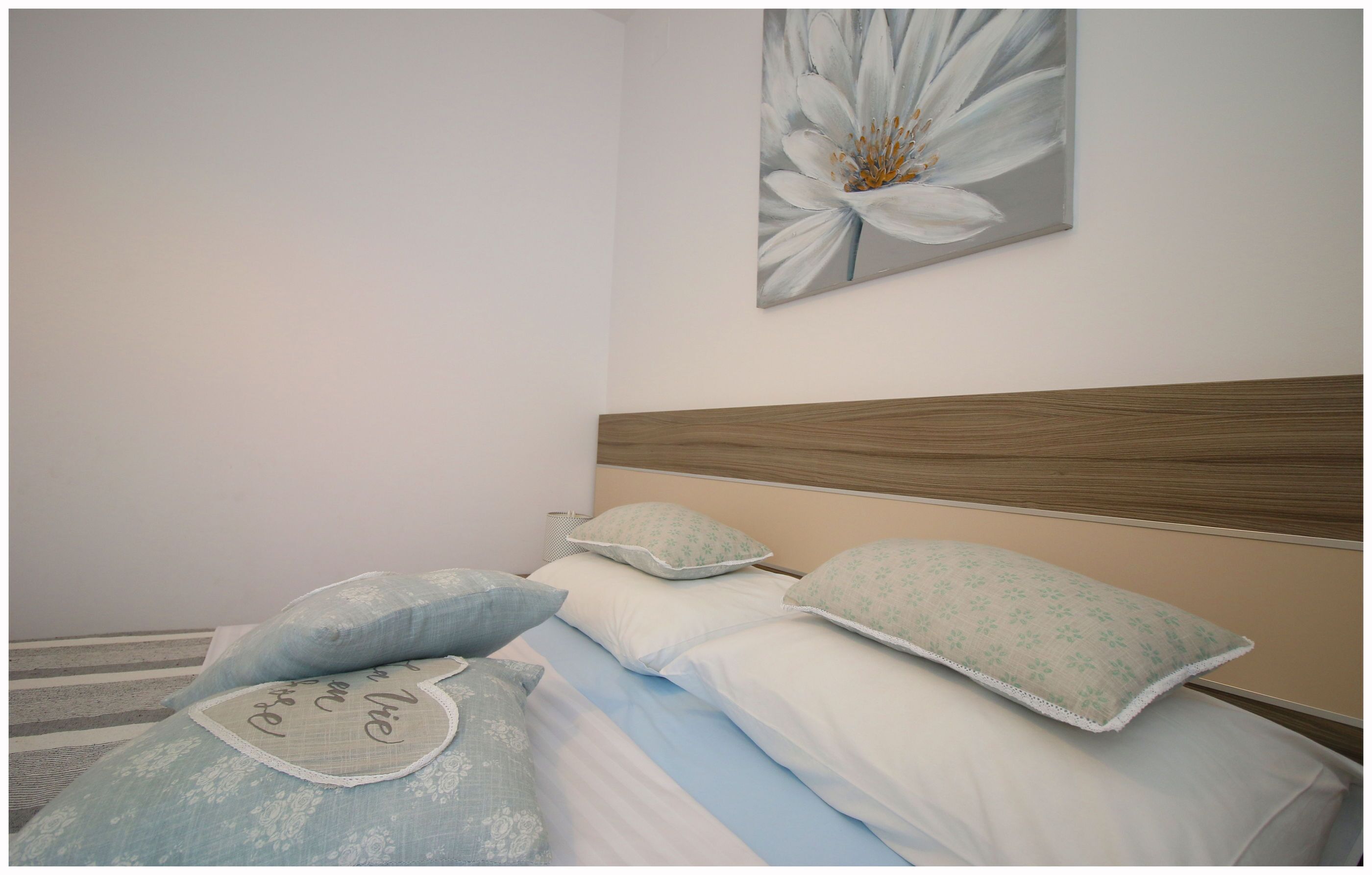 Een net opgemaakt bed met kussens met bloemenprint en een effen wand met een enkel bloemschilderij.