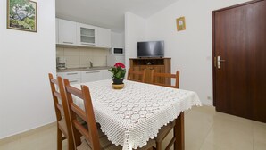 Ein kleines, sauberes Zimmer mit einem Holztisch, Stühlen, einem Fernseher und einer Holztür.