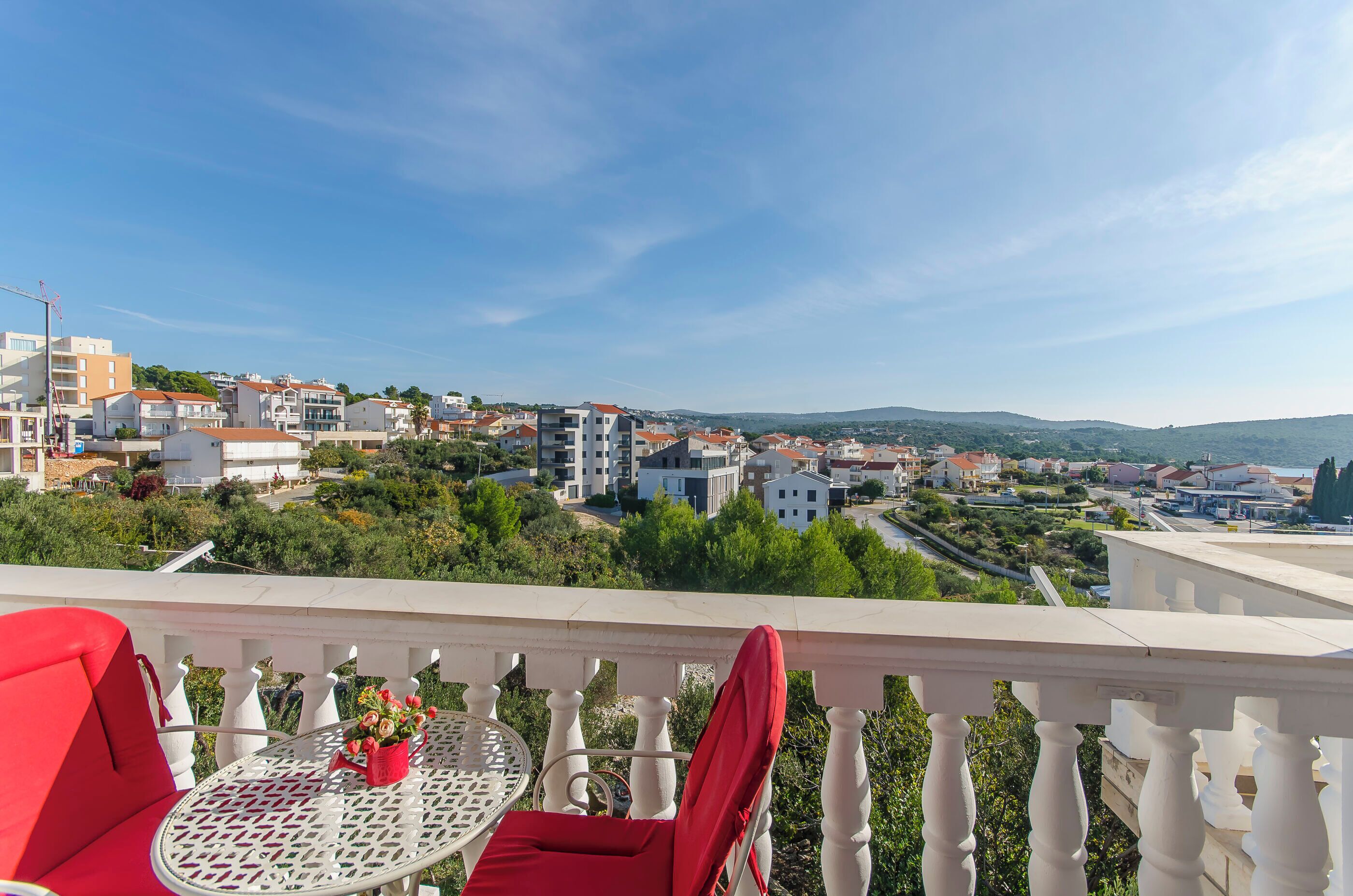 A balcony with a table and chairs, overlooking a residential area with houses and greenery.