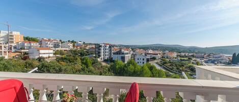 A balcony with a table and chairs, overlooking a residential area with houses and greenery.
