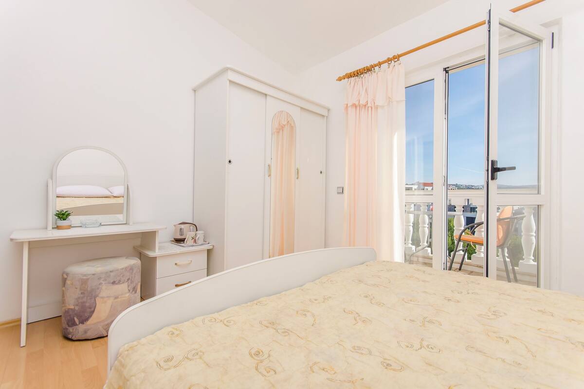 A bedroom with a bed, a desk, a wardrobe, and a balcony with a view.