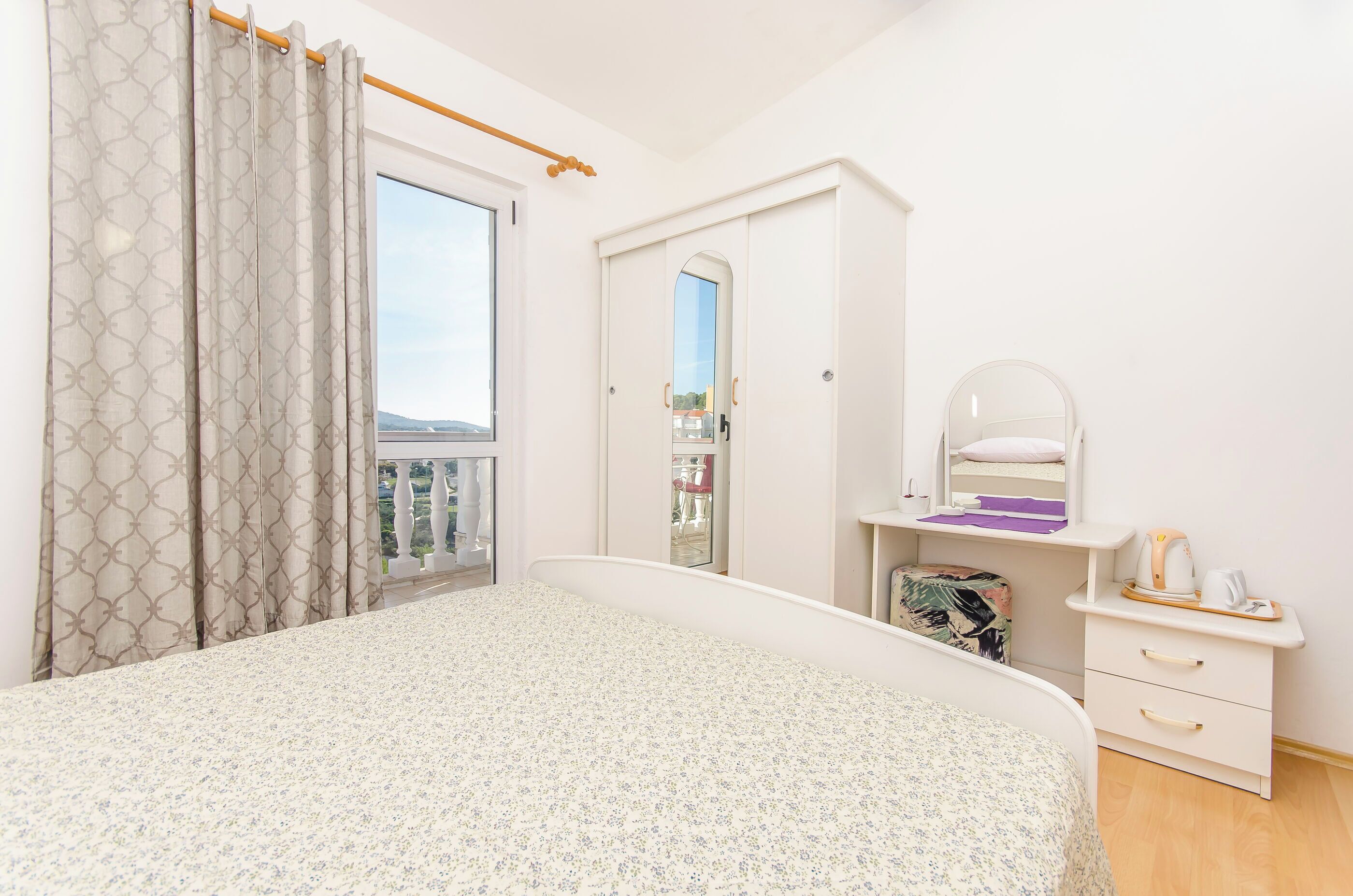 Ein Schlafzimmer mit einem Bett, einem Schminktisch, einem Spiegel und einem Fenster mit Vorhängen.