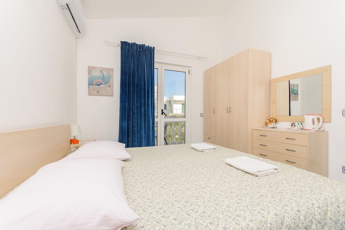 A hotel room with a bed, a wardrobe, a mirror, and a window with curtains.