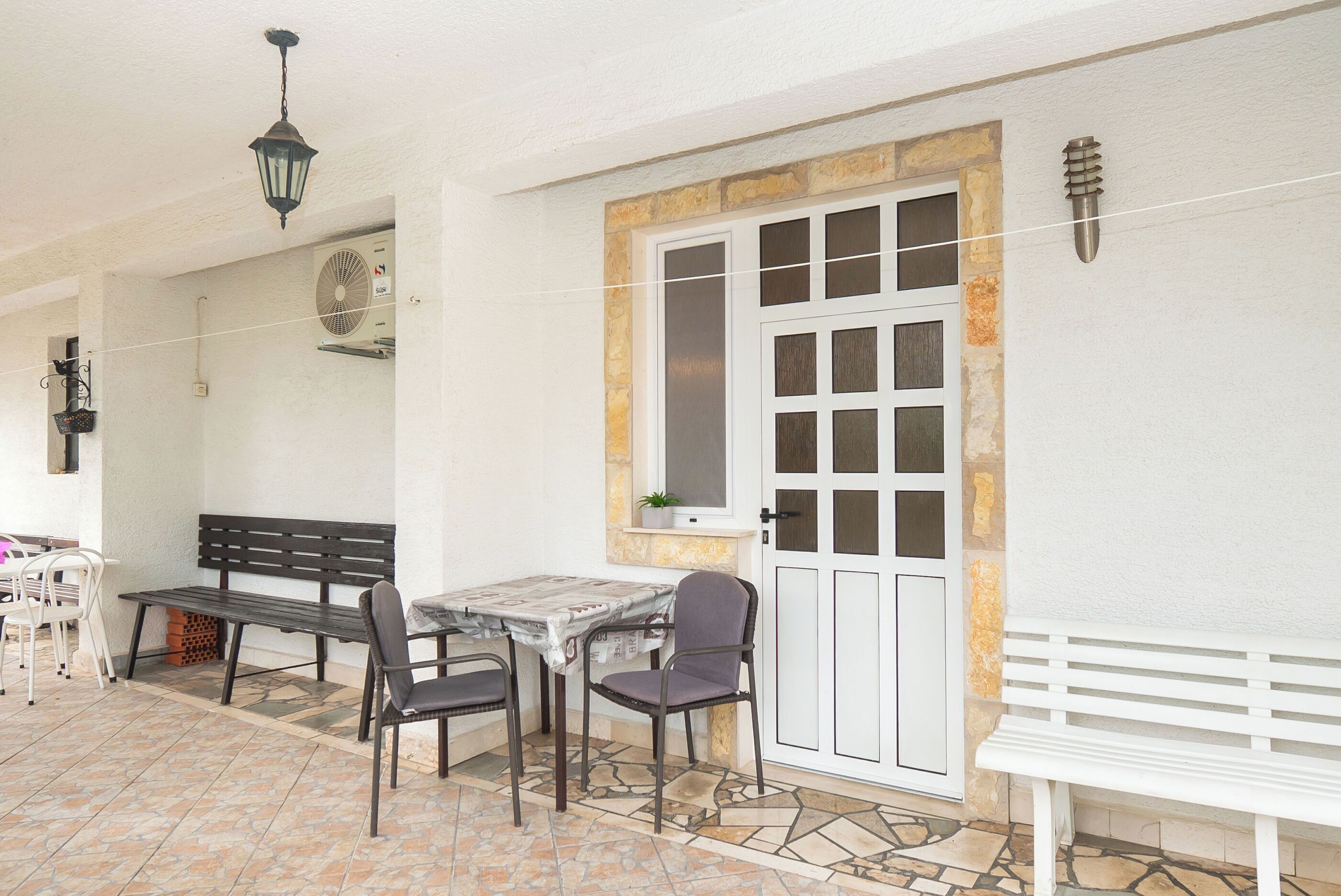 An outdoor patio area with a table and chairs, a bench, a fan, and a door with a stone frame.
