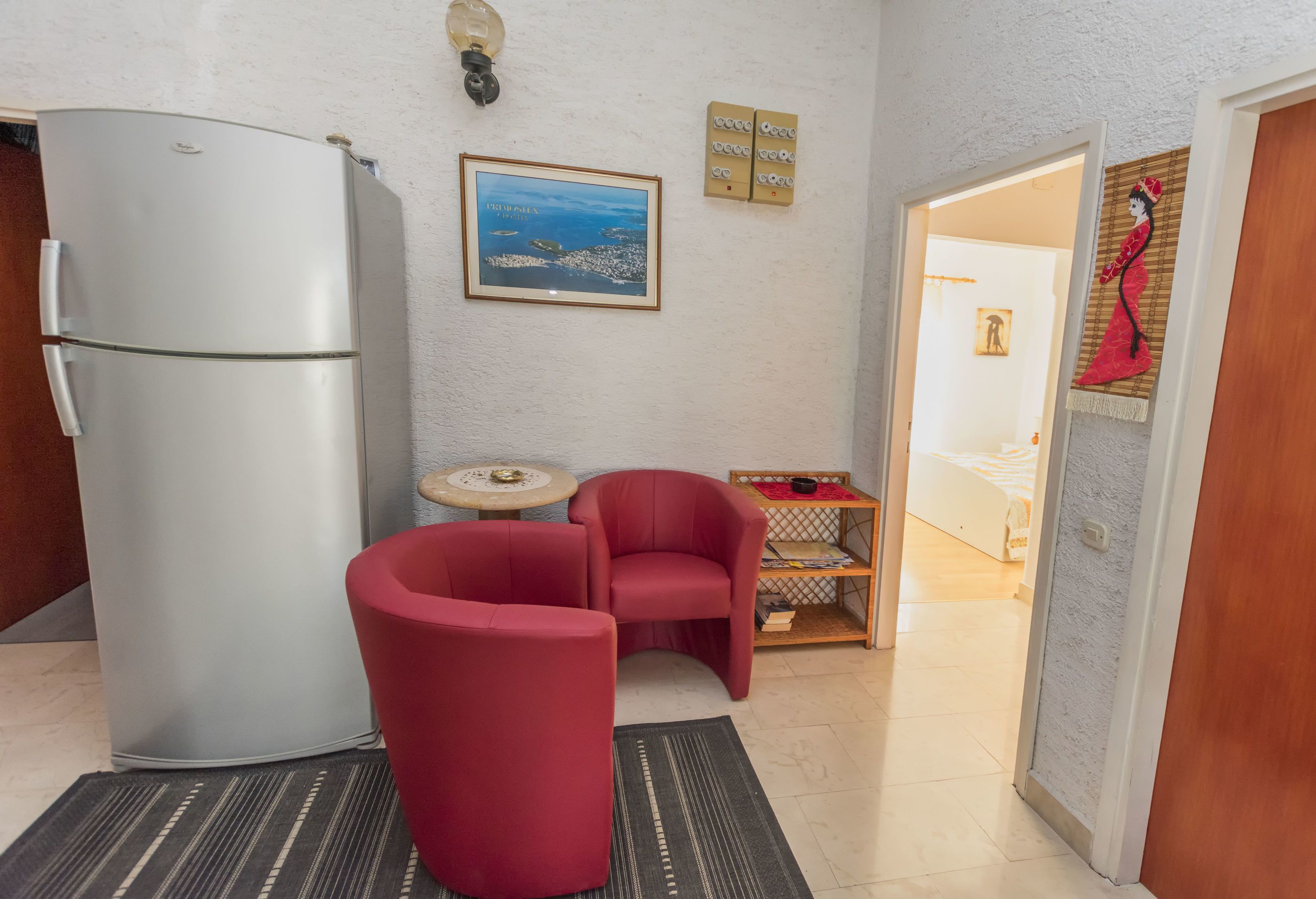 Una cucina compatta con un frigorifero bianco, una sedia rossa, un piccolo tavolo rotondo e un quadro appeso al muro.