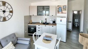 A compact kitchen with a clock, a dining table, and a sofa.