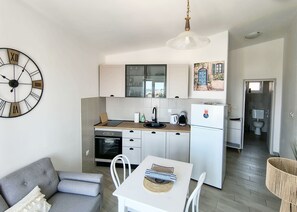 A compact kitchen with a clock, a dining table, and a sofa. - Apartment Nensi (Primosten)