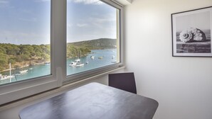Een kamer met een groot raam met uitzicht op een baai met boten en begroeiing.