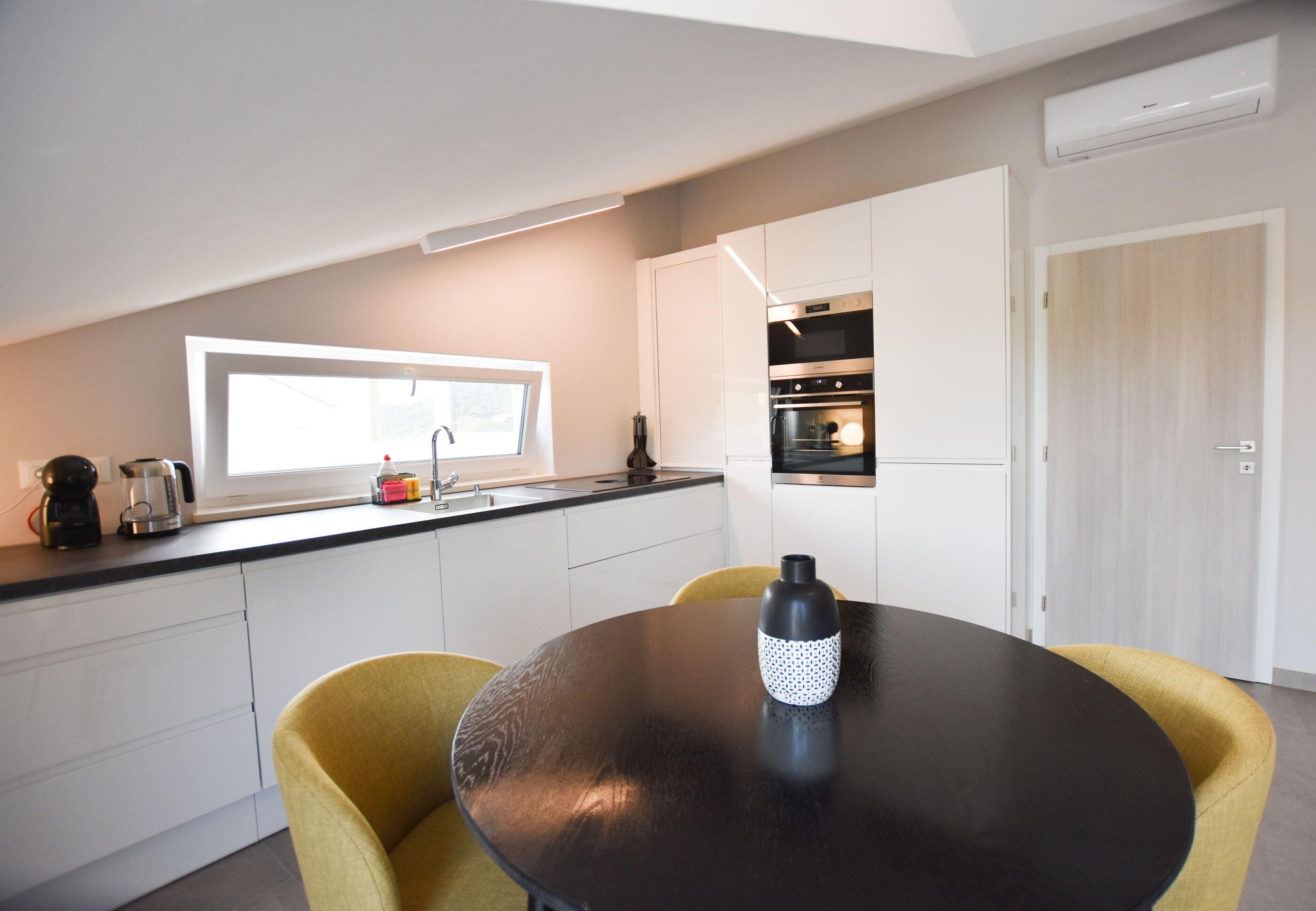 Une cuisine moderne avec des meubles blancs, un plan de travail noir et une table ronde ornée d’un vase aux motifs noirs et blancs.