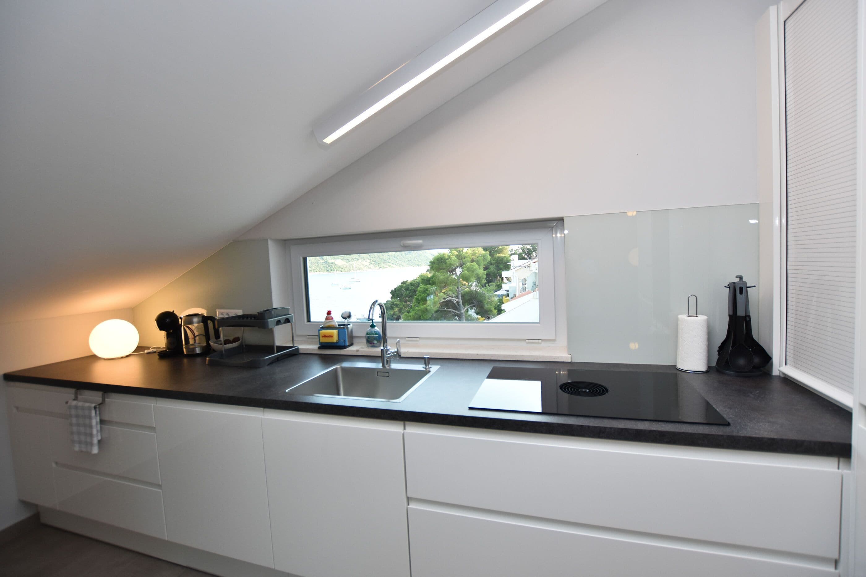 A modern kitchen with a black countertop, white cabinets, a window with a view, and a built-in stove.