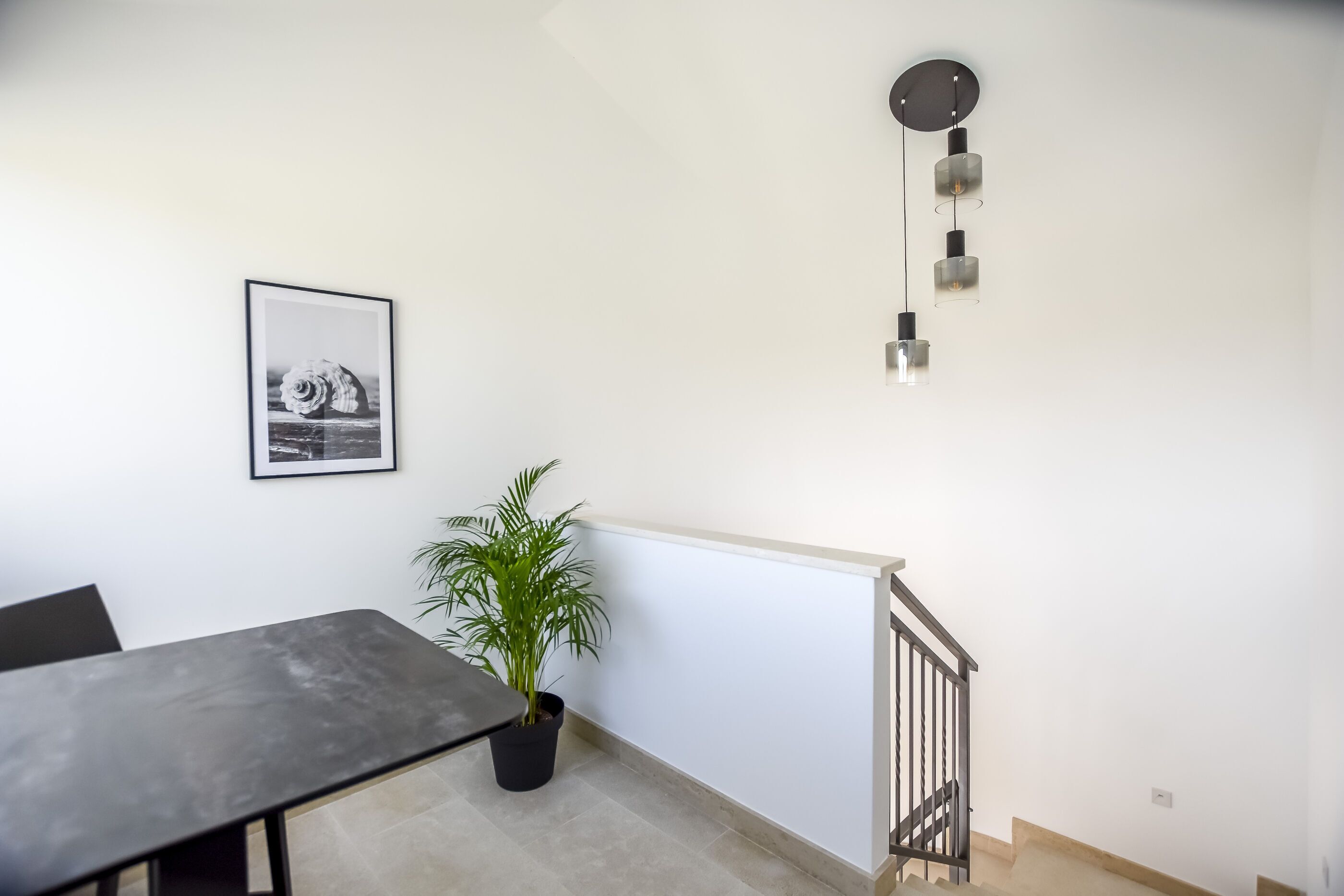A modern room with a dining table, a potted plant, a framed picture, and a staircase.