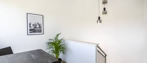 Une pièce moderne comprenant une table à manger, une plante en pot, un tableau encadré et un escalier.