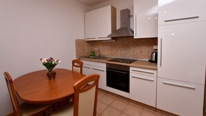 A compact kitchen with white cabinets, a wooden dining table, and a built-in oven. - Apartment Tome (Primosten)