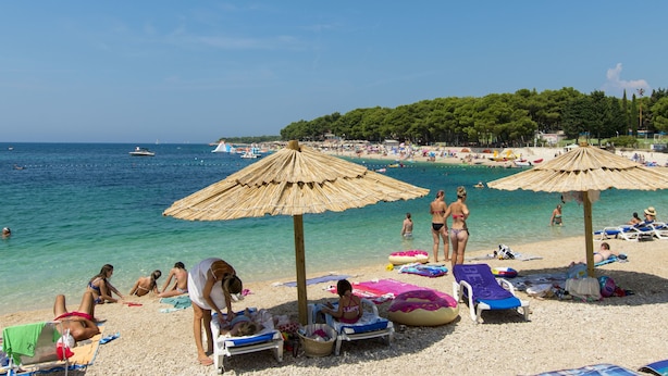 A beach with umbrellas, lounge chairs, and people sunbathing. - Apartment Tome (Primosten)