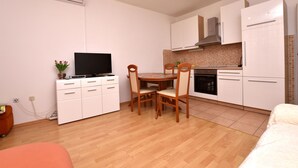 A compact kitchen with white cabinets, a wooden dining table with chairs, a built-in oven, and a TV on a white cabinet. - Apartment Tome (Primosten)