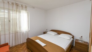 A bedroom with a wooden bed, white bedding, a nightstand with a lamp, and a chair. - Apartment Tome (Primosten)