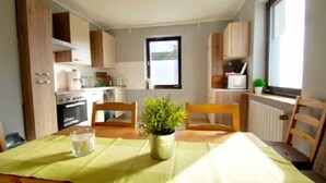 Une cuisine de taille réduite, avec des meubles de rangement en bois, une table à manger avec des chaises, une plante en pot et une fenêtre.