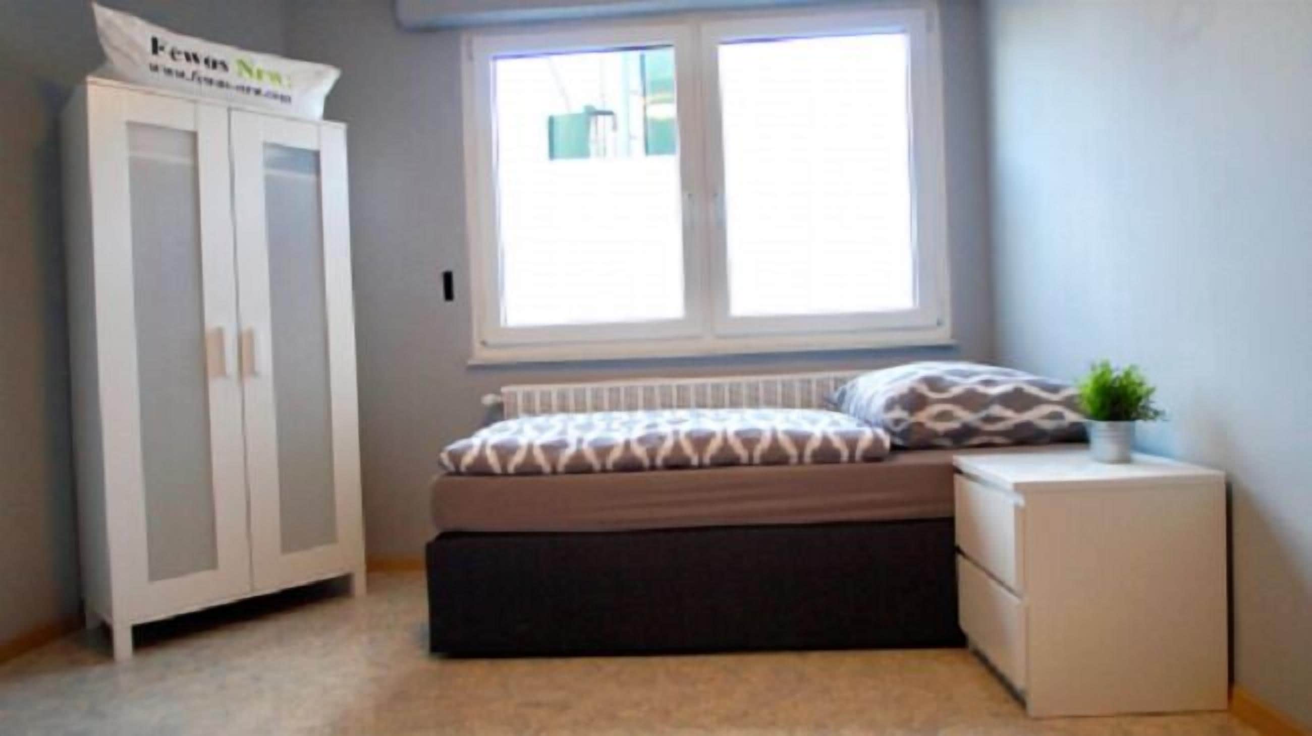 Une chambre à coucher avec un lit, une table de chevet, une armoire et une fenêtre.