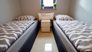 Une chambre avec deux lits, chacun recouvert d’une couvre-lit à motifs zébrés, une petite table de chevet avec un oreiller, et une fenêtre située au-dessus des lits.