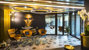 A modern lobby with a large mural, geometric patterned floor, and contemporary furniture. - My Home My Hotel Rosenheim (Rosenheim)