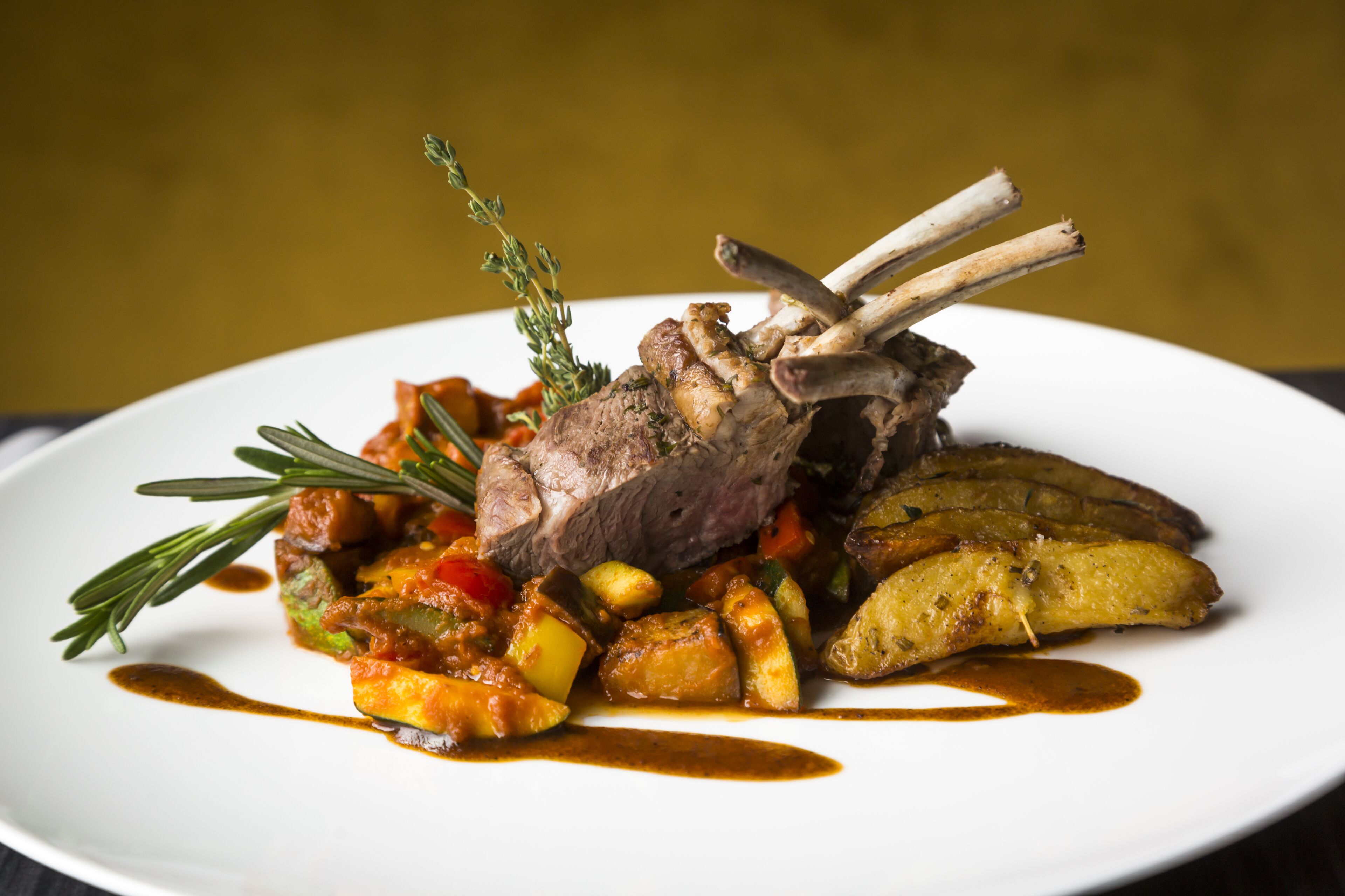 Une assiette de nourriture comprenant un jarret d’agneau, des légumes et des pommes de terre.